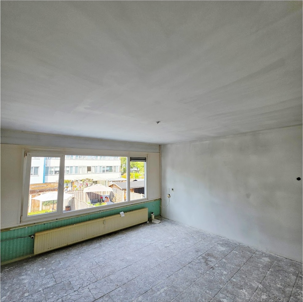 Pas gestuukte woonkamer met een brede raampartij en een groene radiator